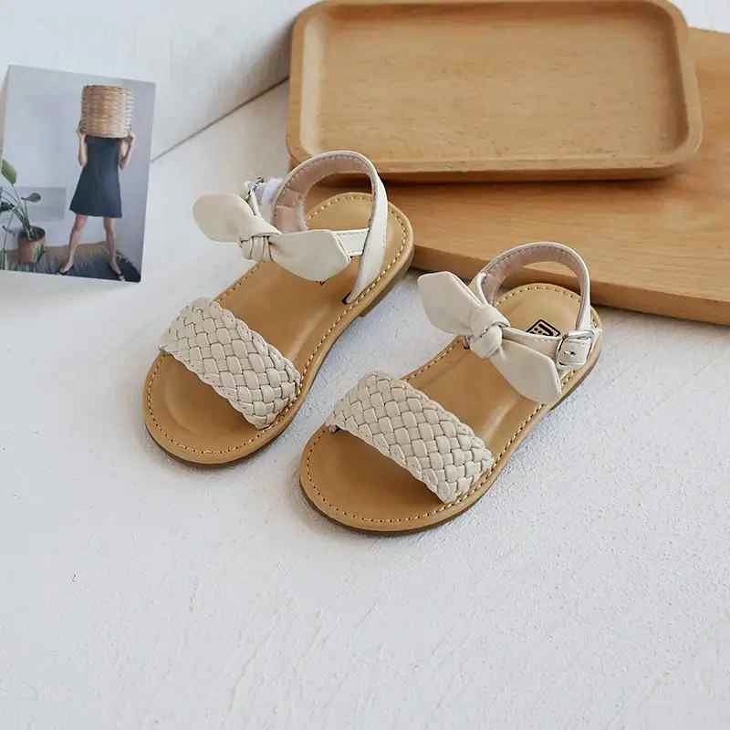 Girls beige flat sandals with woven front strap and bow ankle closure